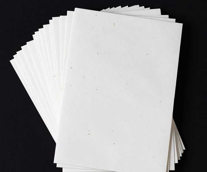 Stack of white blank sheets of paper with subtle speckled texture, fanned out on a black background.