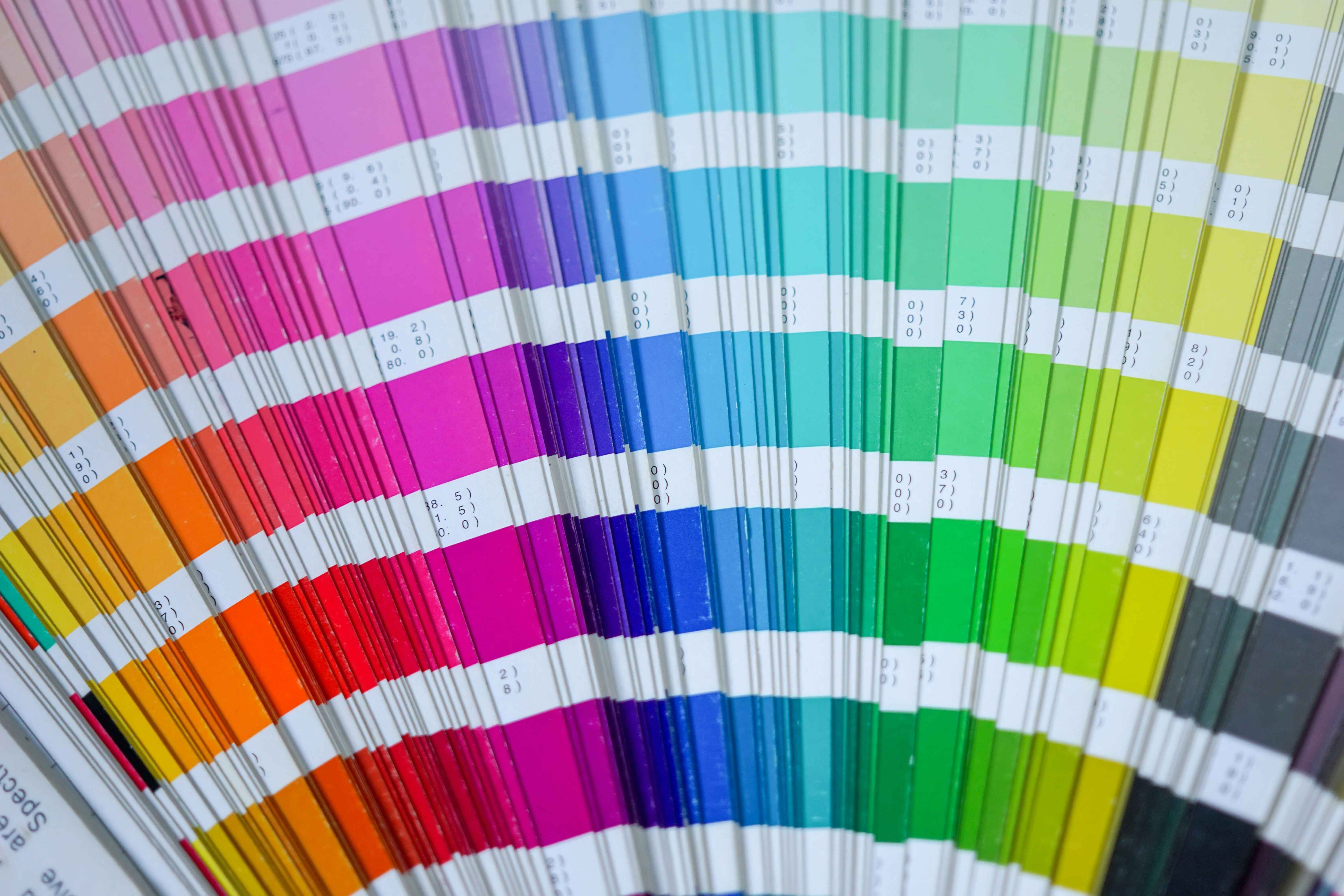 Close-up of a vibrant colour swatch fan displaying a spectrum of colours from warm reds and oranges to cool greens and blues, with accompanying color codes.