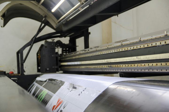 Close-up of an industrial printing machine in operation, producing a large-format print with detailed precision, inside a modern printing facility.